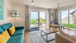 Un salon spacieux avec un canapé de couleur turquoise, une table basse et un fauteuil gris. Une grande fenêtre offre une vue sur l’extérieur.