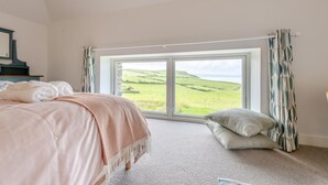 Une chambre avec une grande fenêtre, un lit, une table de chevet et une vue sur un paysage verdoyant.