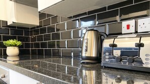 A kitchen with a black tiled backsplash, a stainless steel kettle, and a toaster on a granite countertop.