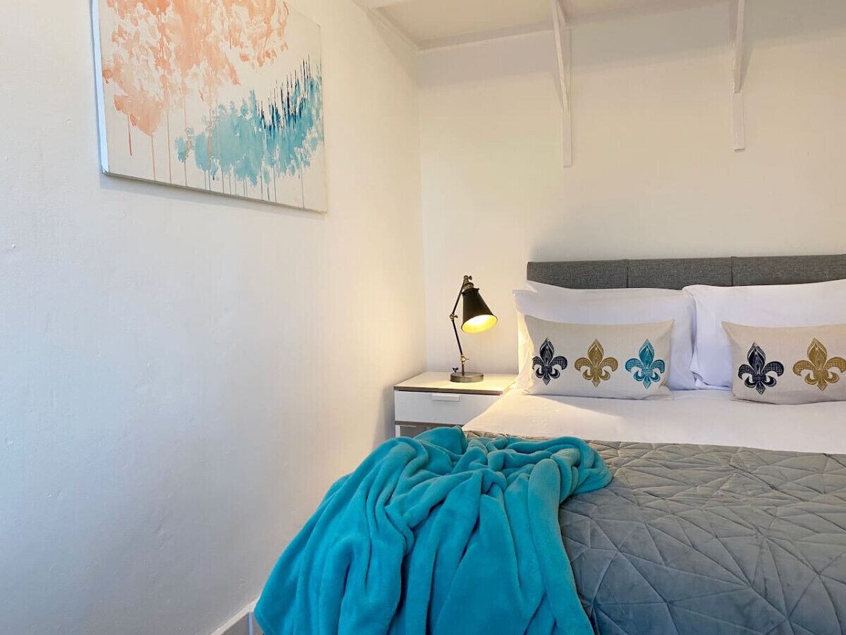 A neatly made bed with a teal blanket, a bedside lamp, and decorative pillows with fleur-de-lis designs.