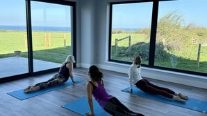 Three people doing yoga on mats in a room with large windows overlooking a grassy field. - 2 Bed in Abbotsham (oc-g28822) (Abbotsham)