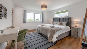 A bedroom with a bed, bedside tables, a desk, a chair, a window, and a hanging light fixture. - 2 Bed in Abbotsham (oc-g28822) (Abbotsham)