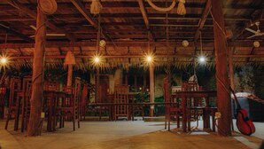 A wooden interior with chairs and a guitar, featuring a thatched roof and hanging lights. - Shell Resort Arugambay (Arugam Bay)
