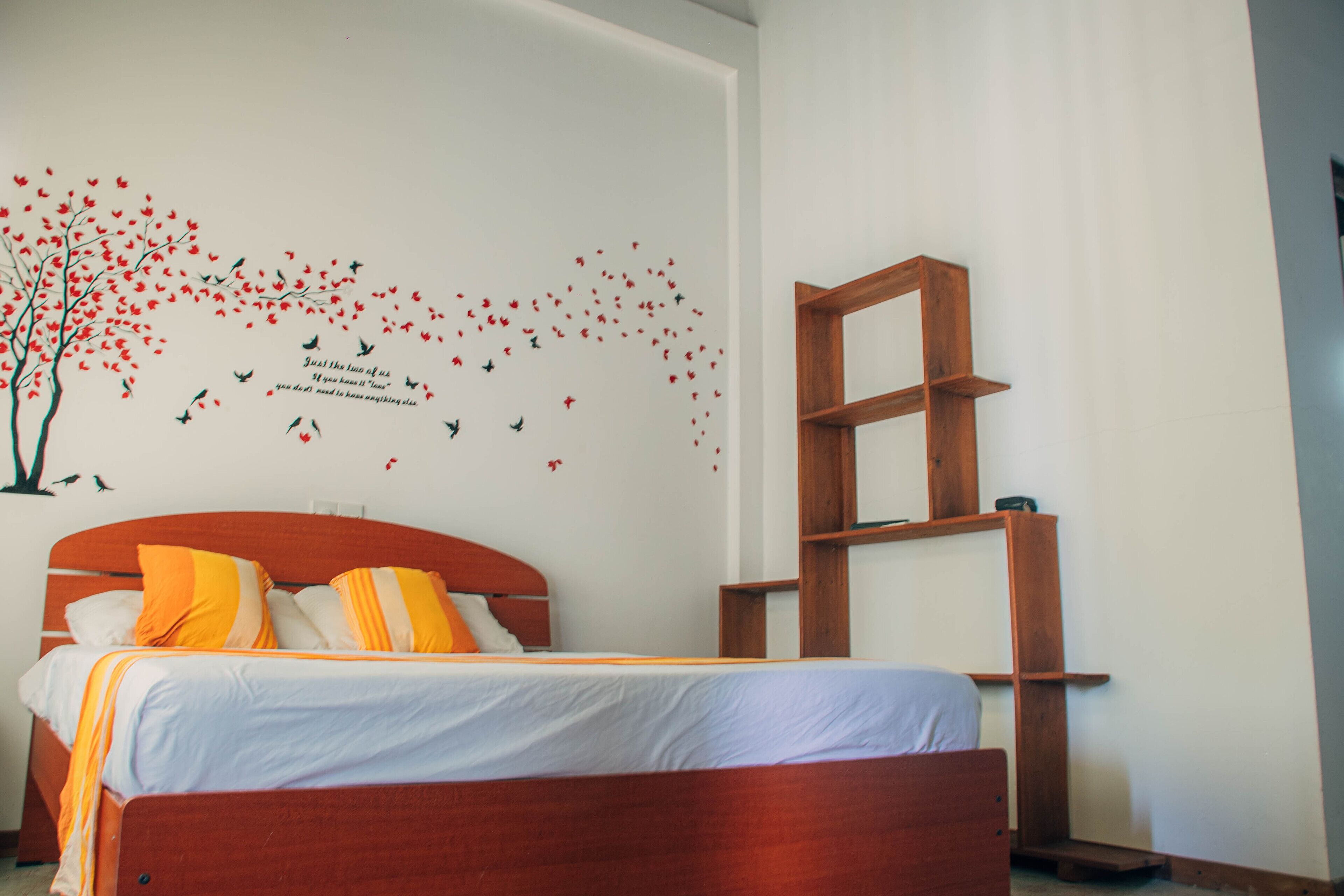 A bedroom with a bed, a wooden headboard, a wall-mounted shelf, and a wall decal of birds and flowers.