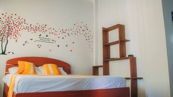 A bedroom with a bed, a wooden headboard, a wall-mounted shelf, and a wall decal of birds and flowers.