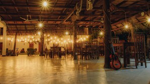 A spacious hall with wooden ceiling beams, hanging lights, and a guitar leaning against a pillar. - Shell Resort Arugambay (Arugam Bay)