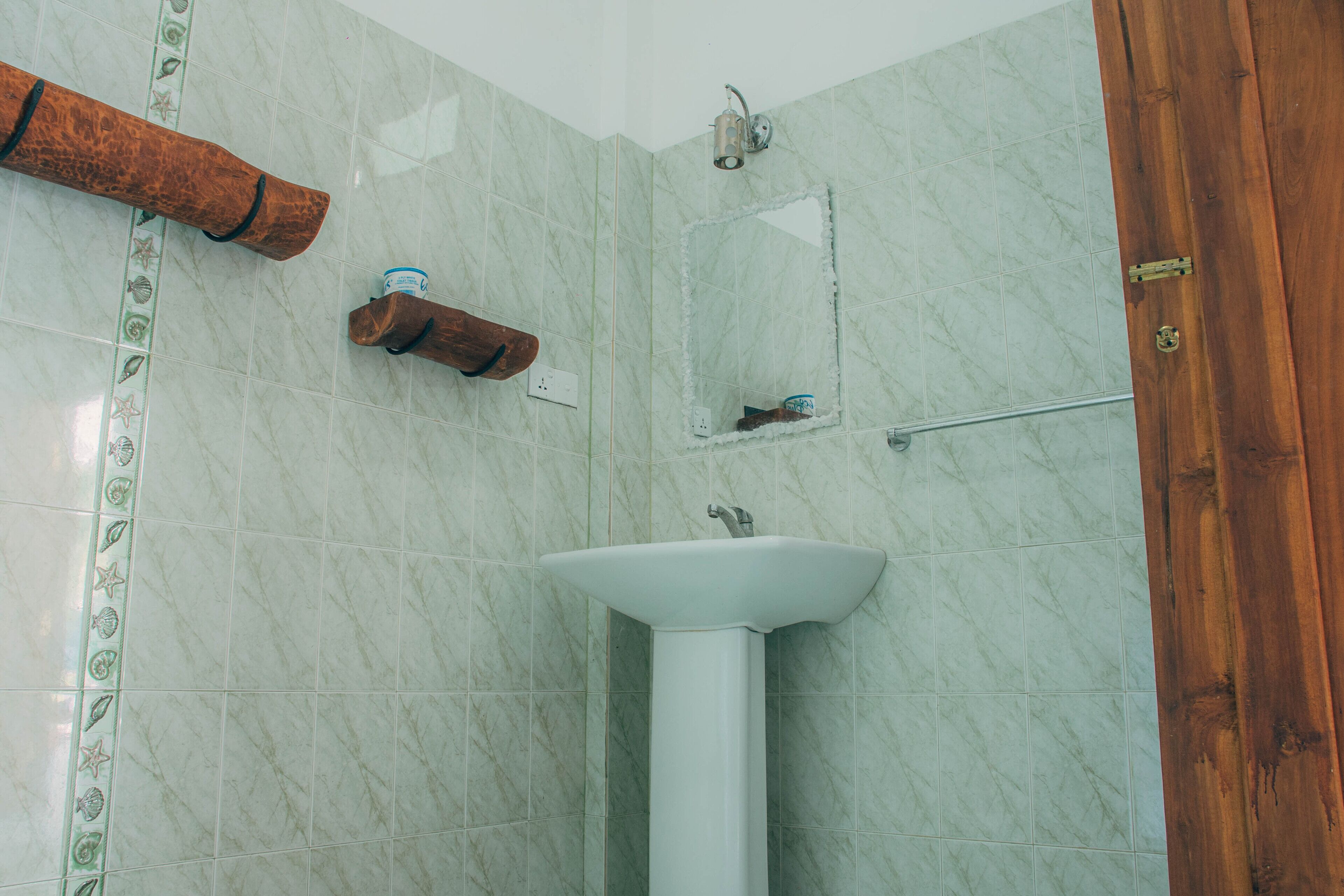 A bathroom with a white pedestal sink, a wooden towel rack, a mirror, and a shower area.