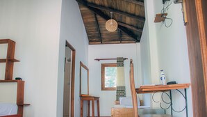 A room with a wooden bed, a small wooden table, a chair, a window with curtains, and a ceiling fan. - Shell Resort Arugambay (Arugam Bay)