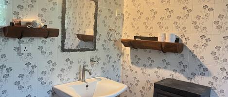 A bathroom with a sink, mirror, and two wooden shelves.