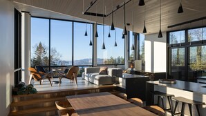 Una cucina moderna con un'isola grande, un tavolo da pranzo in legno e sgabelli da bar. Ampie finestre offrono vista all'esterno.