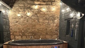 Una habitación con paredes de piedra, una bañera de madera caliente y un pequeño banco de madera.