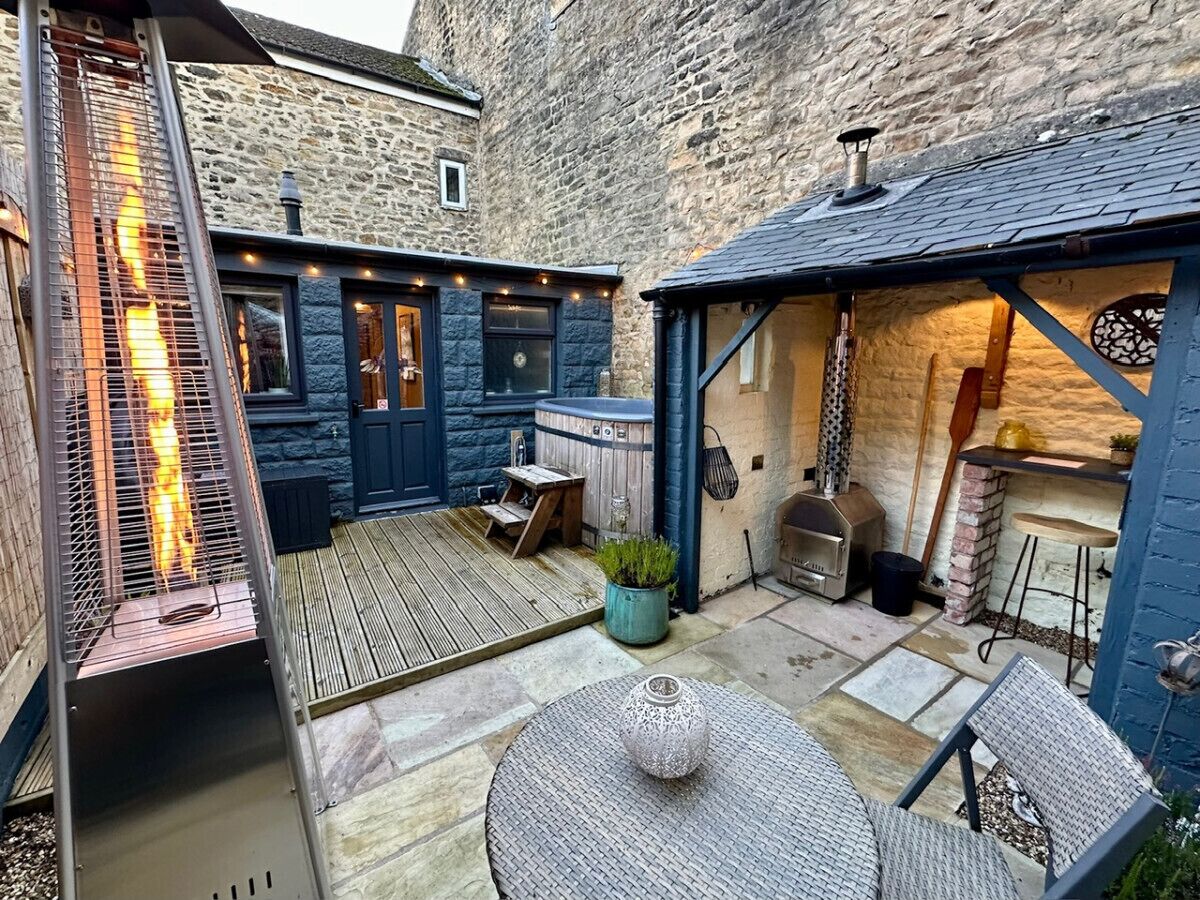 Ein Steinhaus mit einer Holzterrasse, Grillplatz und Sitzgelegenheiten im Freien.