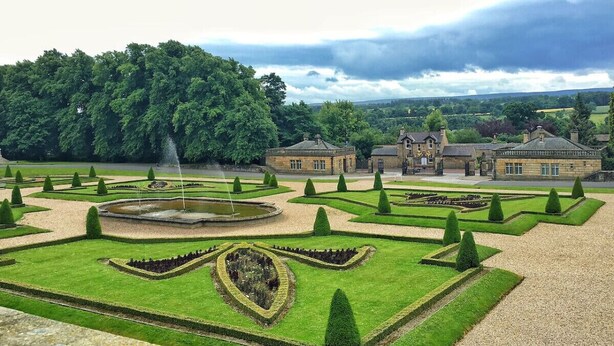 Un jardín formal con diseños geométricos, una fuente y arquitectura clásica.