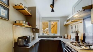 Cocina compacta con armarios oscuros, cafetera y ventana con cortinas.