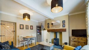 Una sala acogedora con puerta de madera, una mesa de comedor con sillas, un sofá, un sillón amarillo, una chimenea y un televisor.