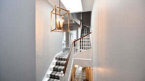 Un escalier moderne agrémenté d’un luminaire aux formes géométriques, d’un tapis à carreaux et offrant une vue sur l’espace cuisine.