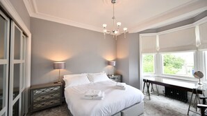 Une chambre à coucher avec un lit, des lampes de chevet, un bureau et une fenêtre donnant sur un beau paysage.