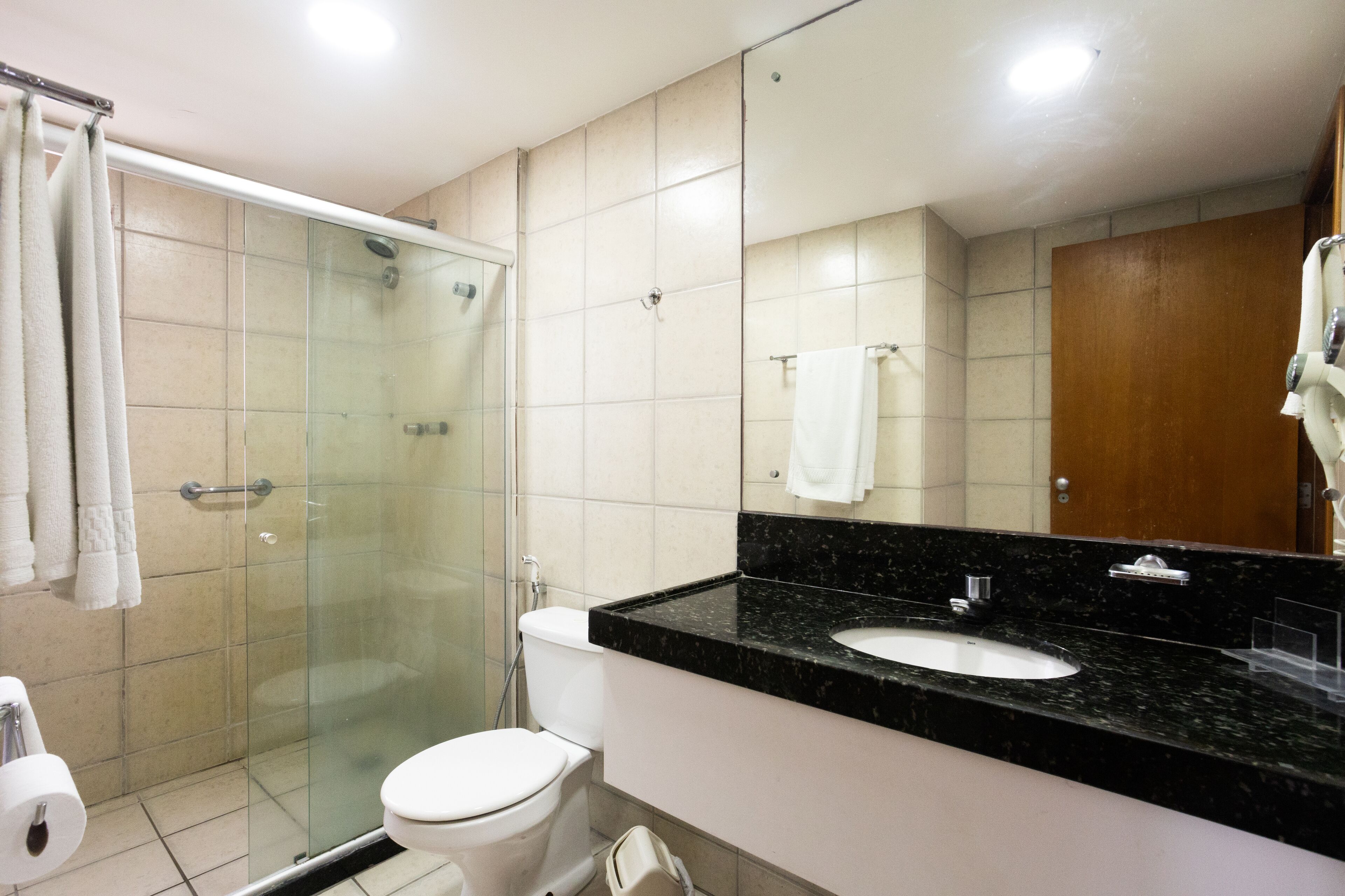 A modern bathroom with a glass-enclosed shower, a white toilet, and a black marble sink.