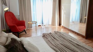 Ein modernes Wohnzimmer mit einem großen Spiegel, einem roten Sessel, einem kleinen runden Tisch und einem beigen Teppich.