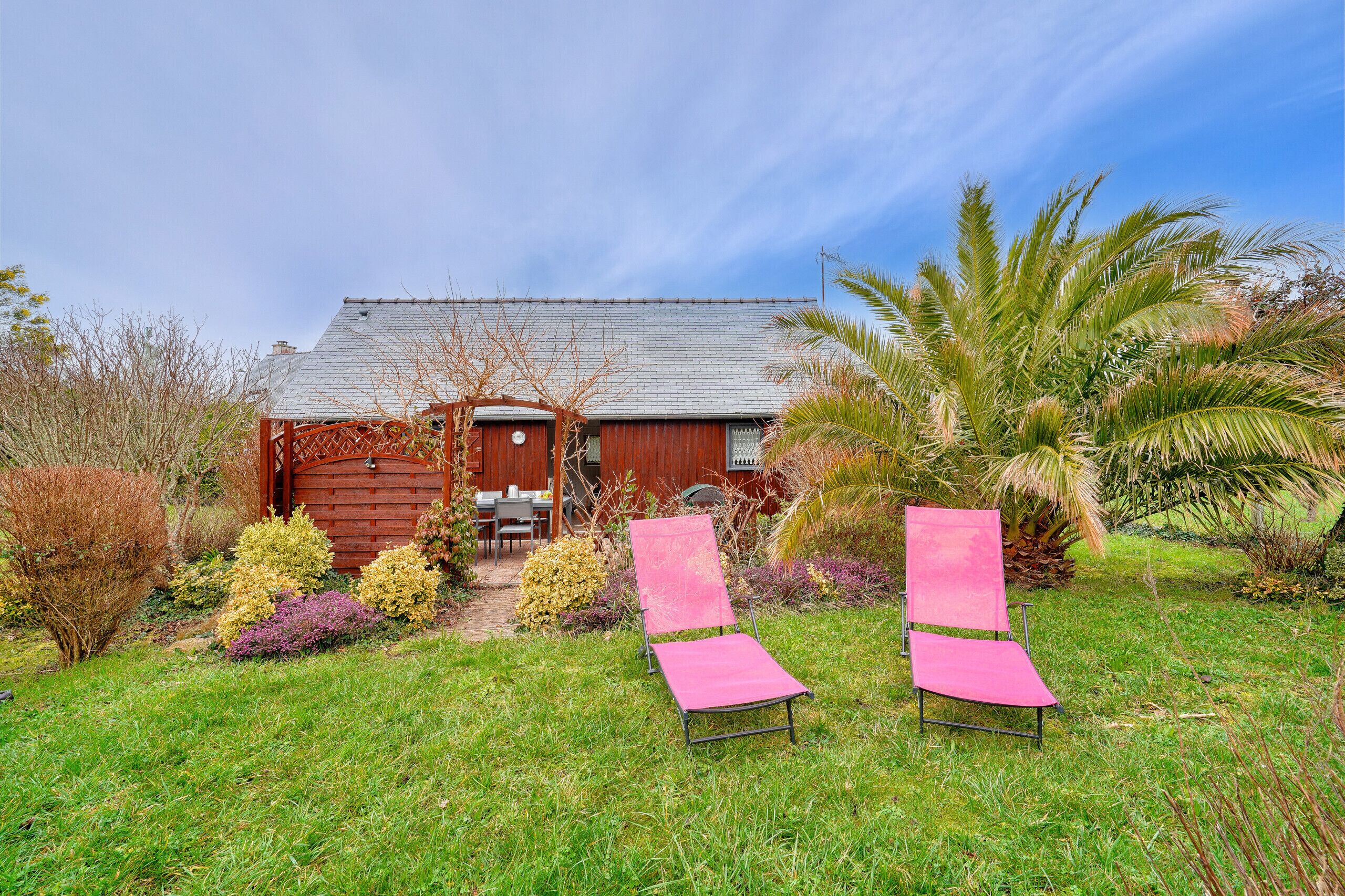 Una casa con jardín, dos sillones reclinables rosados y una valla de madera.