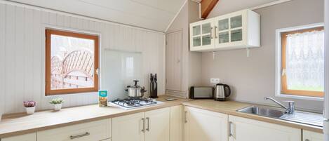A kitchen with white cabinets, a gas stove, a sink, and a window with a view of a wooden deck.