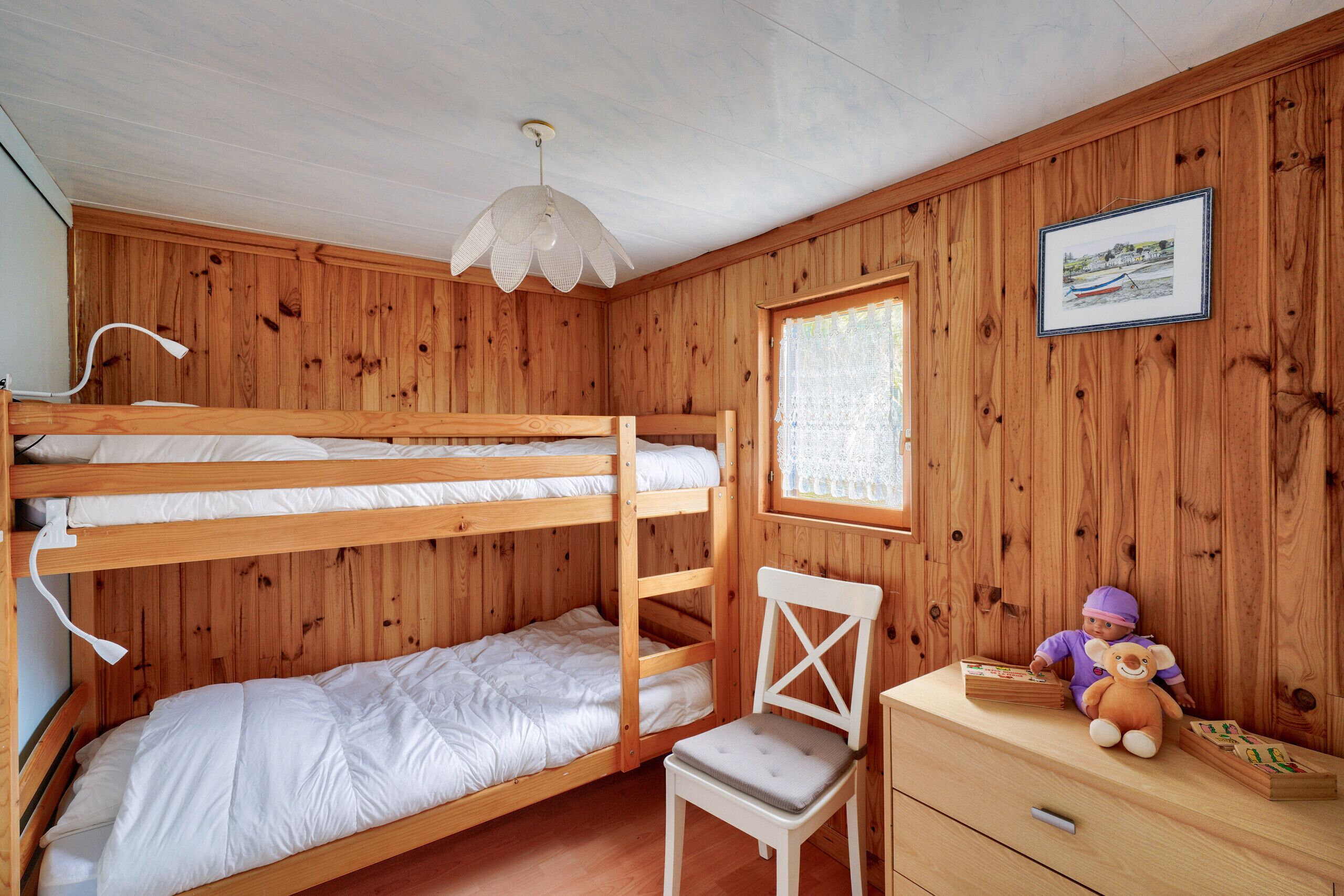 A bunk bed room with a desk and chair, a lamp, and a framed picture on the wall.