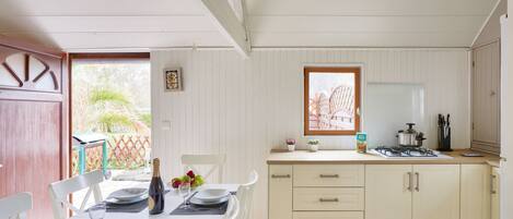 A dining area with a table set for four, a kitchen with a stove and sink, and a window with a view of palm trees.