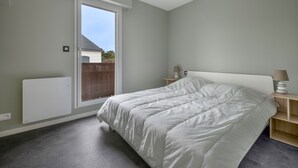 Un dormitorio con una cama grande, una mesita de noche con lámpara, una ventana y un radiador.