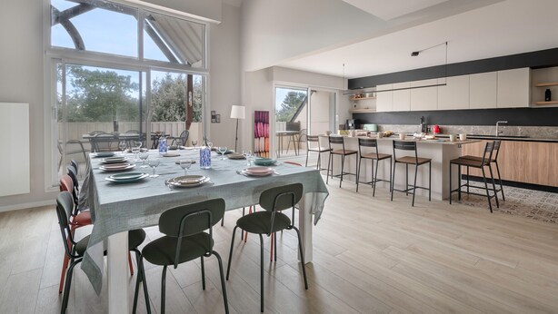 Una cocina moderna con una isla grande, taburetes de bar y un comedor con una mesa larga y sillas.