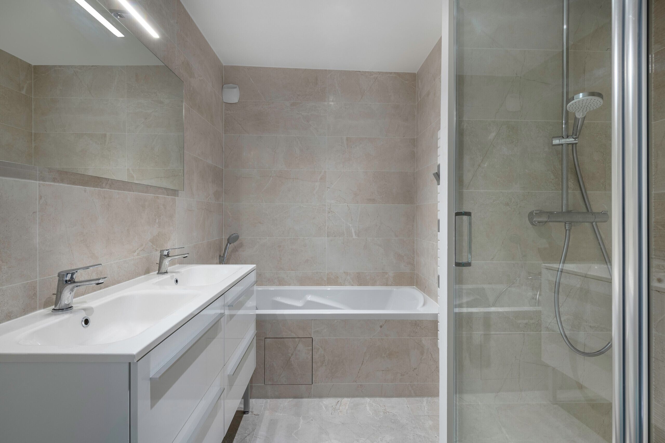A modern bathroom with a glass-enclosed shower, a double sink vanity, and beige tiles.