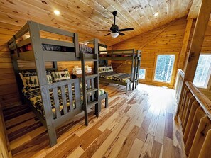 A cabin with bunk beds, a ceiling fan, and a view of trees through the window. - 65PT New Log Cabin in Private Setting. Hot tub, Fire pit, Gym/Pool Access, and Dog Friendly! (Twin Mountain)