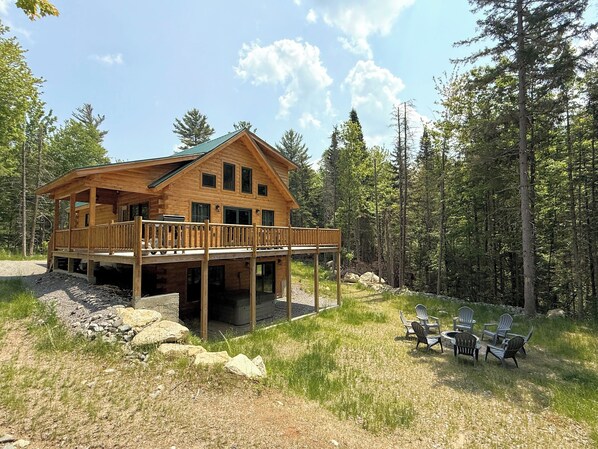 A wooden cabin with a deck and outdoor seating area. - 65PT New Log Cabin in Private Setting. Hot tub, Fire pit, Gym/Pool Access, and Dog Friendly! (Twin Mountain)