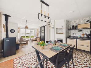 A modern kitchen with a brick wall backsplash, a dining area with a wooden table, and a visible outdoor view through large windows. - Flat for 4 with large garden (Préfailles)