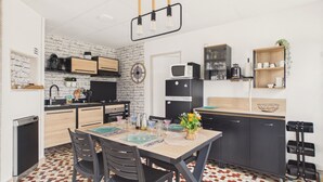 A compact kitchen with a dining area, featuring a tiled floor, modern appliances, and a brick wall. - Flat for 4 with large garden (Préfailles)