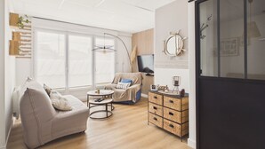 A modern living room with a sofa, armchair, and a coffee table. There is a television, a large window, and a sliding door. - Flat for 4 with large garden (Préfailles)