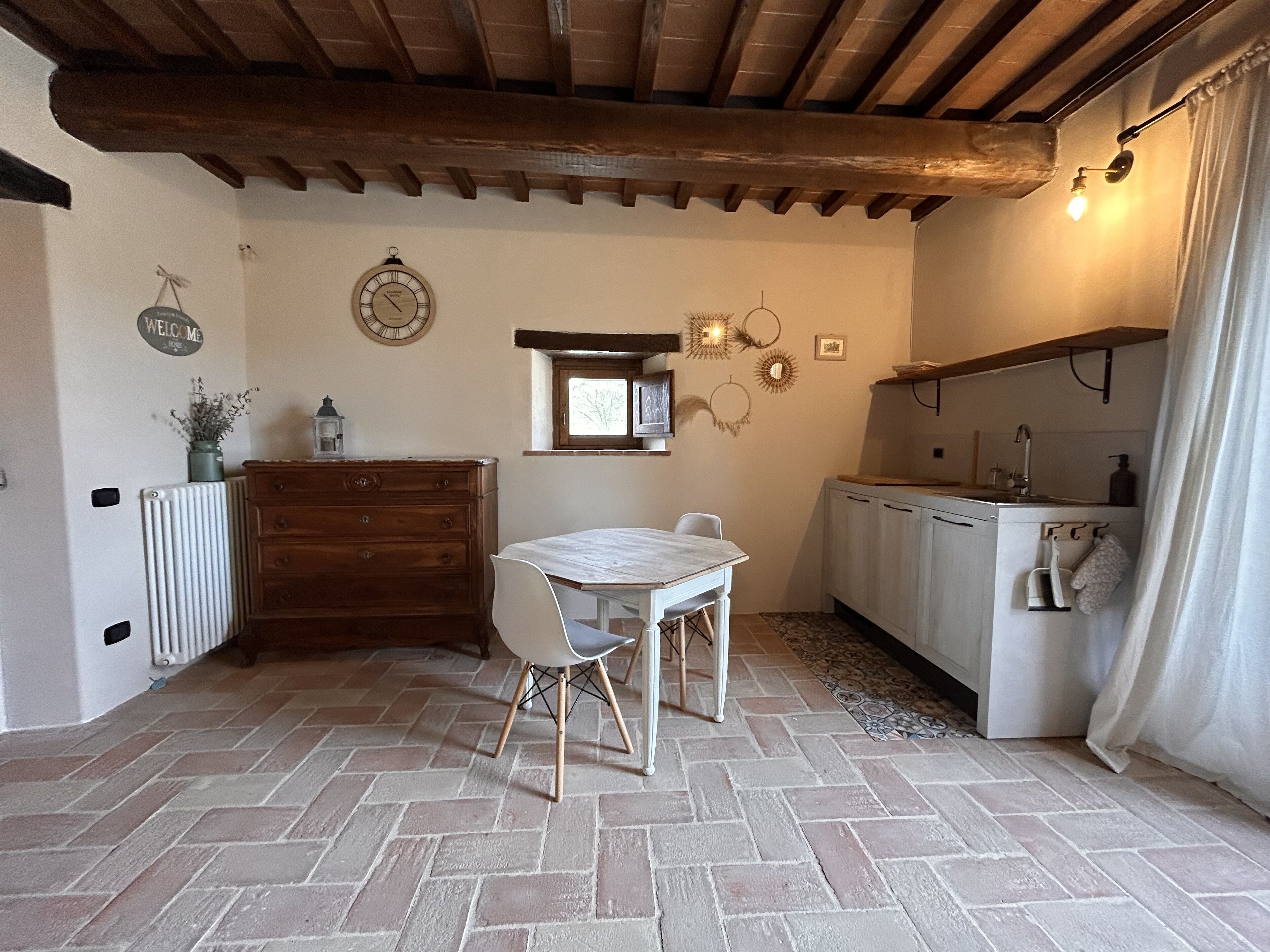A rustic kitchen with a wooden table and chairs, a built-in oven, and a window above the sink.