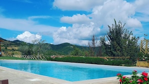Piscina com deck de pedra, rodeada por vegetação e colinas ao fundo.