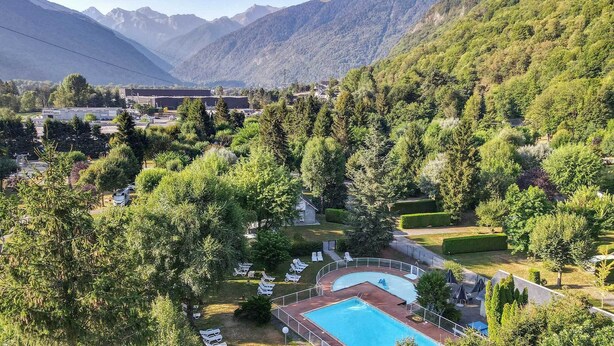 A resort with a swimming pool surrounded by lush greenery and mountains in the background. - Camping Pradelongue (Moustajon)