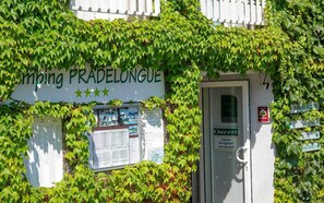 A building with ivy covering the walls, a sign reading "Camping PRADELONGUE", and a door labeled "Ouvert". - Camping Pradelongue (Moustajon)