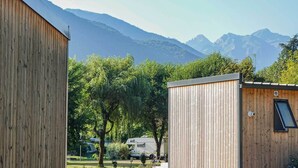 A wooden cabin with a window and a door, surrounded by trees and a mountain backdrop. - Camping Pradelongue (Moustajon)