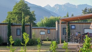 A rustic cabin with a wooden exterior, a covered patio, and a mountain backdrop. - Camping Pradelongue (Moustajon)
