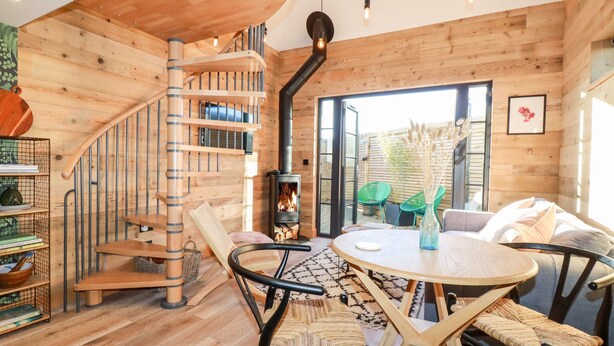 A wooden interior with a spiral staircase, a round dining table, and a fireplace. - Little Beach Cabin (Newquay)