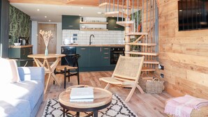 A modern loft with a spiral staircase, a kitchen, and a living area with a sofa and a coffee table. - Little Beach Cabin (Newquay)