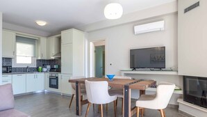 Een moderne keuken met witte kasten, een eettafel met stoelen, een televisie boven de open haard, en een klein keukeneiland met waterkoker.