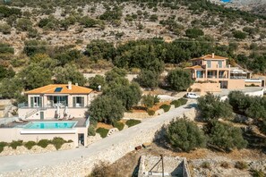 Una casa de dos pisos con piscina, rodeada de árboles y terreno rocoso.