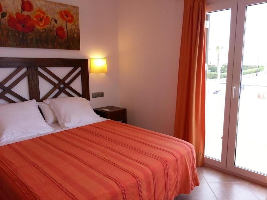 A hotel room with a bed, a nightstand, a painting, and a sliding glass door to the outside.