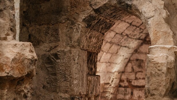 Un antiguo arco de piedra que da paso a una habitación con suelo de baldosas y una mesa con sillas.