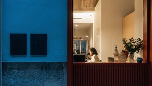 Un área de recepción con mostrador de madera, dos placas en la pared y una planta a la derecha.