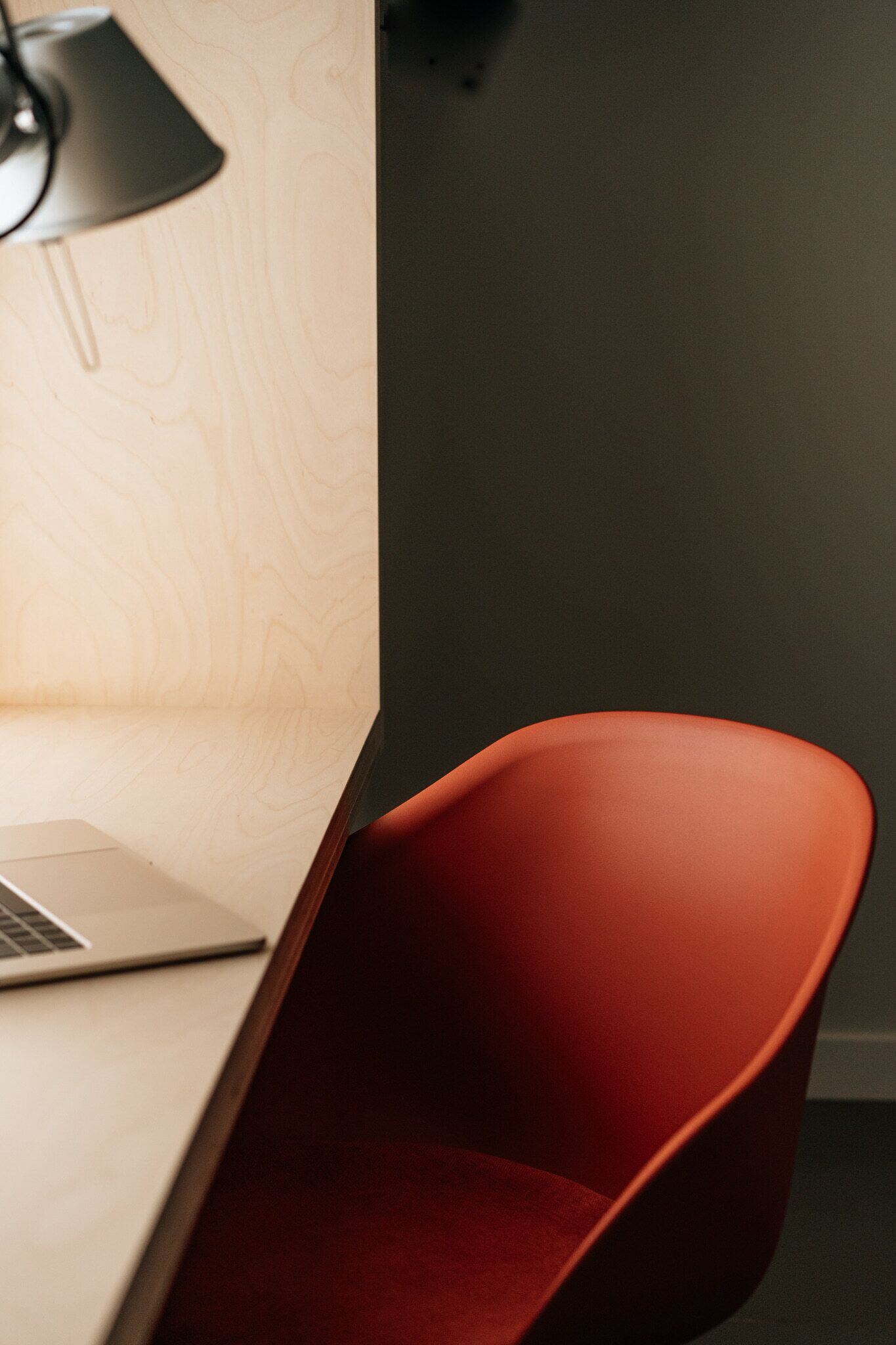 Una habitación moderna con una pared de madera, una silla roja y un ordenador portátil sobre un escritorio.