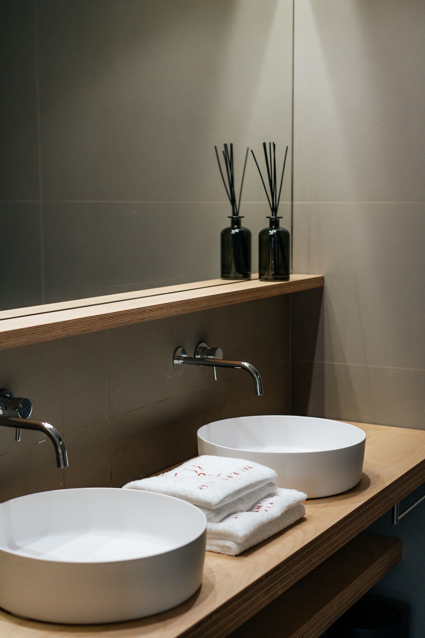 A bathroom with two round white sinks, a wooden vanity, and a mirror above the sinks.